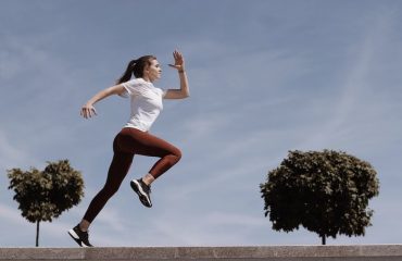 Athletic woman running on an outdoor road, demonstrating fitness and determination under a blue sky.