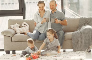 Cheerful family wearing casual clothes sitting in living room while playing and drinking tea during weekend at home in morning